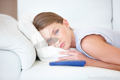 Image of Sad, relax and a woman watching tv on a sofa in the living room of her home for entertainment. Face, depression and remote with a young person streaming a video, movie or film in her apartment