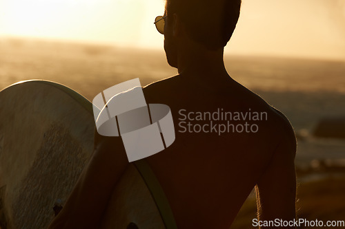 Image of Man, beach and surf, sunset and silhouette with back view, sport and travel, adventure and fitness in nature. Ocean, orange and peace with freedom, workout on summer vacation and surfboard outdoor