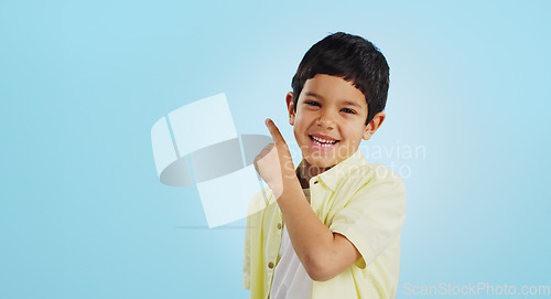 Image of Boy, smile and pointing with excitement in studio on blue background in mockup for opportunity, deal or alert. Youth, kid and happy with offer, discount or announcement on social media for consumers