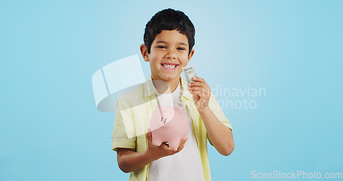 Image of Piggy bank, cash and child face with money, savings and cash planning in a studio, Happy, portrait and young boy with allowance and safe for bills, wealth and budget with blue background and smile