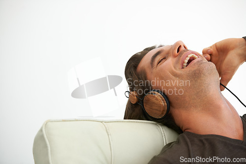 Image of Headphones, happy and young man relaxing on chair in studio listening to music, radio or playlist. Smile, technology and male person streaming song or album and chilling isolated by white background.