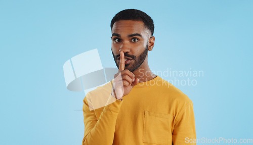 Image of Secret, face and man with finger on lips in studio for quiet, privacy or hush news on blue background. Whisper, drama and portrait of guy model with confidential hand emoji for gossip or announcement