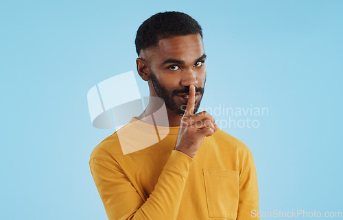 Image of Secret, face and man with finger on lips in studio for quiet, privacy or hush news on blue background. Whisper, drama and portrait of guy model with confidential hand emoji for gossip or announcement