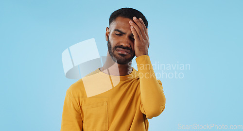 Image of Stress, fail and man in studio with facepalm emoji for stupid mistake or regret on blue background. Anxiety, oops and male model with disaster, crisis or fake news shame, frustrated and unhappy