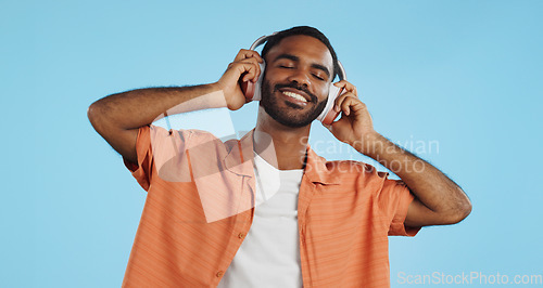 Image of Black man, headphones and dancing to music with happiness and energy in studio on blue background. Techno, rave and fun with audio streaming, dancer is excited with smile and wireless technology