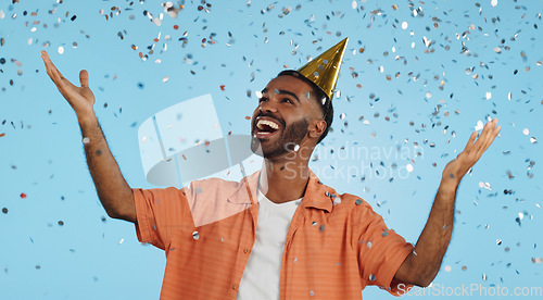 Image of Man, birthday party hat and confetti in studio, smile or surprise for celebration by blue background. Person, event and excited with silver glitter, achievement or happy for winning with wow for goal