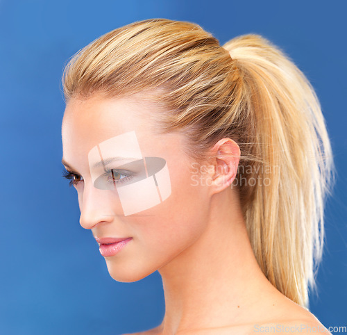 Image of Face, beauty and hair of a woman closeup in studio on a blue background for skin wellness or cosmetics. Aesthetic, skincare and ponytail with a young model profile at the salon for dermatology