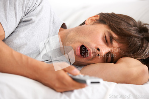 Image of Tv, yawn and tired man in bed with remote control for streaming movies in his home. Fatigue, relax and morning lazy male in a bedroom with television, show or film while on vacation in his house