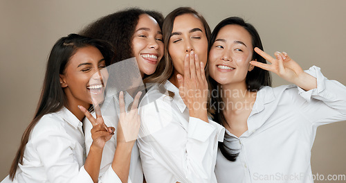 Image of Diversity, peace sign and group of women in studio for empowerment, wellness and community. Emoji, friends and people hug, blow kiss and smile for beauty, inclusion and support on brown background