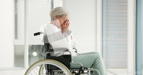 Image of Sad, senior woman and person with disability, wheelchair and crying into hands at the hospital, window or nursing home. Depressed, mental health and elderly person frustrated, thinking in retirement