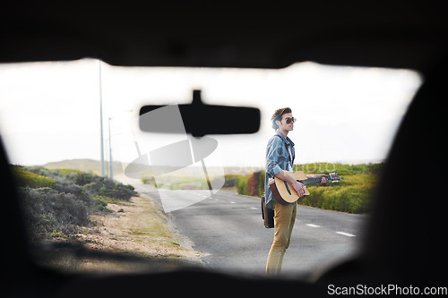 Image of Musician, travel and man with a guitar on a road trip, journey or playing instrument in countryside on highway. Guitarist, trekking and guy waiting outdoor on street for a car, van or transportation