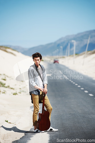 Image of Musician, travel and man with a guitar on a road trip, journey or tour in the countryside on highway. Guitarist, trekking and portrait of guy waiting on street for a car, van or transportation