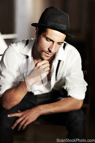 Image of Man, hipster and thinking about fashion, ideas or choice of clothes in dark background. Clothing, decision and creative person or model sitting and planning outfit with vintage hat and retro style