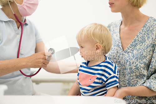 Image of Infant baby boy child being examined by his pediatrician doctor during a standard medical checkup in presence and comfort of his mother. National public health and childs care care koncept.