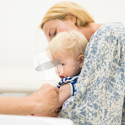 Image of Child beeing vaccinated by pediatrician in presence of his mother. Preventive vaccination against Diphtheria, whooping cough, tetanus, hepatitis, haemophilus influenzae, pneumococcus, poliomyelitis