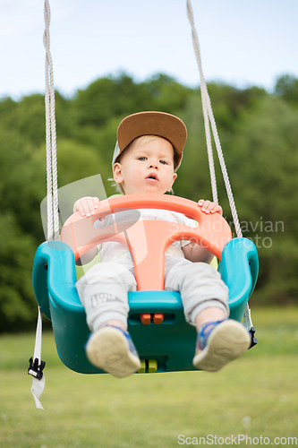 Image of Adorable little happy Caucasian infant baby boy child swinging on playground outdoors.