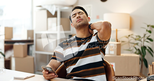 Image of Man, neck pain and phone in office for business in e commerce, logistics or distribution with strain. Asian entrepreneur, tired and sore back at desk with mobile for telecom, social media or internet