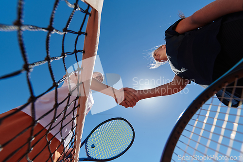 Image of Two female tennis players shaking hands with smiles on a sunny day, exuding sportsmanship and friendship after a competitive match.