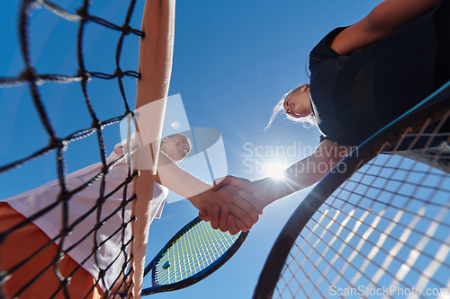 Image of Two female tennis players shaking hands with smiles on a sunny day, exuding sportsmanship and friendship after a competitive match.