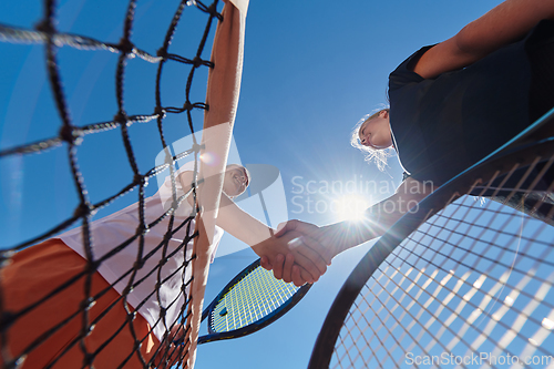 Image of Two female tennis players shaking hands with smiles on a sunny day, exuding sportsmanship and friendship after a competitive match.