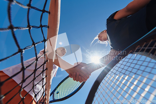 Image of Two female tennis players shaking hands with smiles on a sunny day, exuding sportsmanship and friendship after a competitive match.