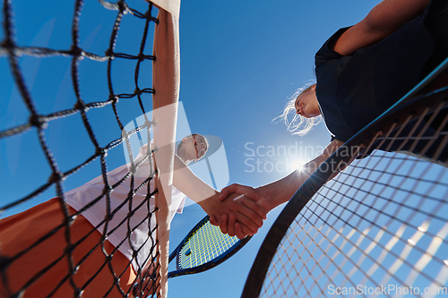 Image of Two female tennis players shaking hands with smiles on a sunny day, exuding sportsmanship and friendship after a competitive match.