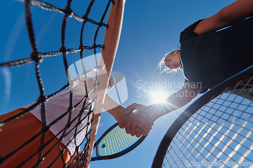 Image of Two female tennis players shaking hands with smiles on a sunny day, exuding sportsmanship and friendship after a competitive match.