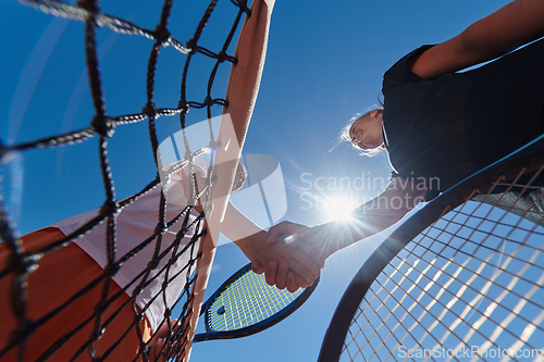 Image of Two female tennis players shaking hands with smiles on a sunny day, exuding sportsmanship and friendship after a competitive match.