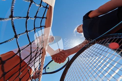 Image of Two female tennis players shaking hands with smiles on a sunny day, exuding sportsmanship and friendship after a competitive match.