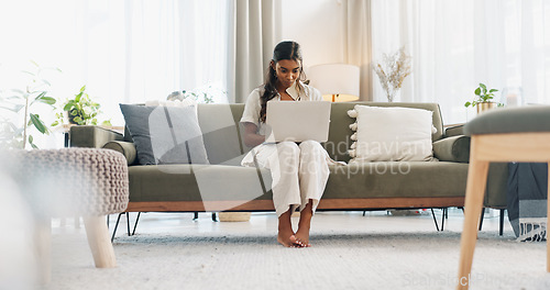 Image of Woman, laptop and typing on sofa for communication, email or social media scroll in living room of home. Indian, girl and pc for freelance web search, streaming or technology with internet in lounge