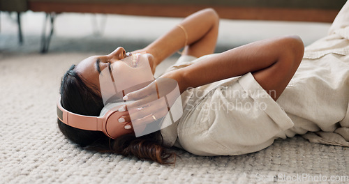 Image of Headphones, relax and young woman in the living room laying on the mat listening to music. Smile, calm and Indian female person streaming podcast, radio or playlist and chilling on the floor at home.