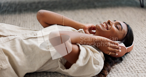 Image of Headphones, smile and young woman in the living room laying on the mat listening to music. Relax, calm and Indian female person streaming podcast, radio or playlist and chilling on the floor at home.