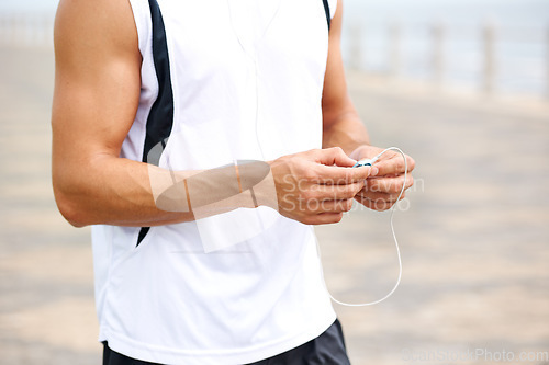 Image of Man, workout and earphones to listen to music, podcast and song on run, exercise and cardio. Male athlete, hearing and streaming radio, audio and sound by ocean, outdoors and inspiration for fitness