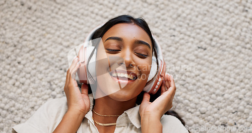 Image of Headphones, happy and young woman on the carpet on the floor listening to music or album. Smile, calm and Indian female person streaming podcast, radio or playlist and chilling in living room of home