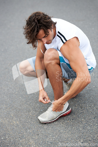 Image of Man, fitness and tie sneakers on road outdoor for running, workout and start sports performance. Runner, earphones and lace shoes on feet to prepare for exercise, cardio and marathon in city street