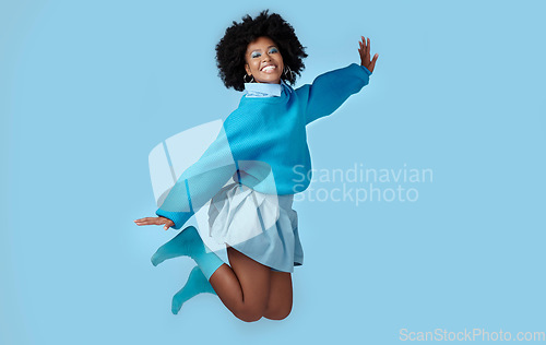 Image of Blue, jump and happy black woman in a studio with trendy, cool and stylish clothes with a background. Happiness, smile and portrait of a young african model with energy, excited and joy.