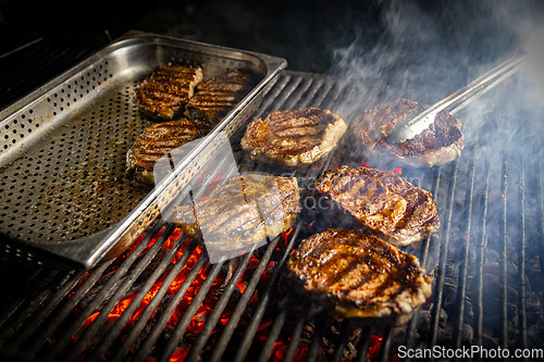 Image of Rib-eye steaks cooking on flaming grill.