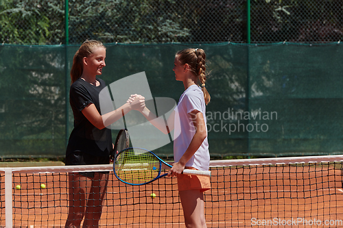 Image of Two female tennis players shaking hands with smiles on a sunny day, exuding sportsmanship and friendship after a competitive match.