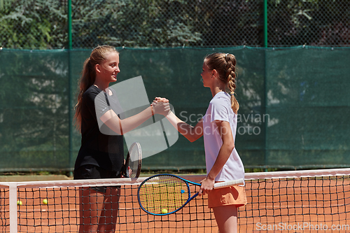 Image of Two female tennis players shaking hands with smiles on a sunny day, exuding sportsmanship and friendship after a competitive match.