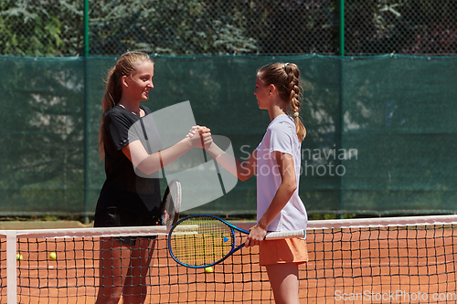 Image of Two female tennis players shaking hands with smiles on a sunny day, exuding sportsmanship and friendship after a competitive match.