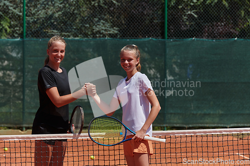 Image of Two female tennis players shaking hands with smiles on a sunny day, exuding sportsmanship and friendship after a competitive match.