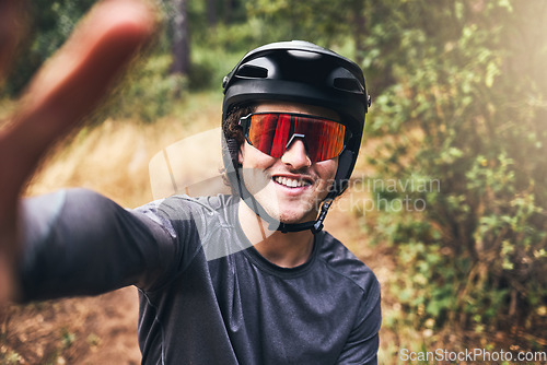Image of Man taking a selfie while cycling on a nature trail, wearing a helmet and sunglasses. Portrait of a cyclist on bicycle ride through a park or forest taking a picture smiling and wearing safety gear