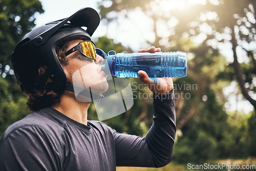 Image of Cyclist, water and bottle in forest for hydration, with cycling equipment and sunglasses by trees for wellness. Man, drink and sports while exercise, workout or training for fitness outside in woods