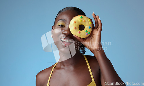 Image of Beauty, black woman and portrait of donut on face with blue studio wall for happy summer style. Matching, beautiful and fun african american girl with yellow makeup for quirky fashion campaign.