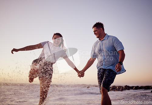 Image of Beach water splash, couple and happy people together feeling love and fun in summer at sunset. Girlfriend and boyfriend holding hands in the ocean waves and sea on a vacation with quality time