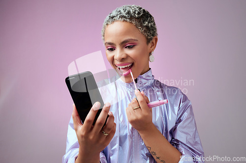 Image of Fashion, phone and woman using lipstick in studio for beauty, makeup and mouth cosmetics routine alone. Social media influencer applying pink lip gloss for selfcare against a grey studio background