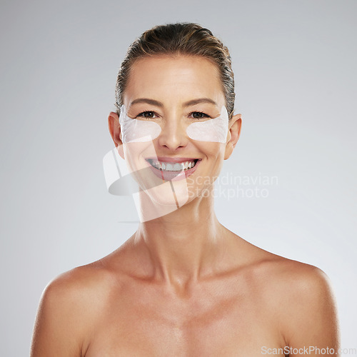 Image of Eye wellness, skincare and mature woman at beauty dermatology spa against a grey mockup studio background. Portrait of an elderly model with smile and happy about luxury gel patches for eyes