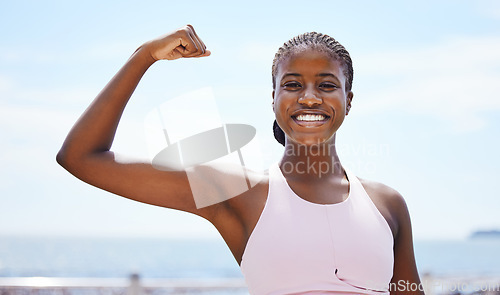 Image of Fitness, portrait and black woman flexing muscle at the beach in summer after strength training, exercise and workout. Smile, motivation and happy girl outdoors with healthy and strong arm biceps