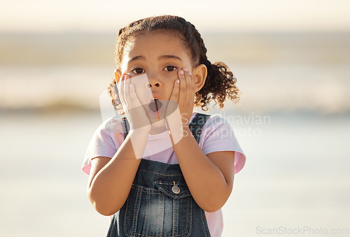 Image of Wow, children and hands on the face of a girl on the beach looking surprised or shocked outside during summer. Kids, youth and surprise with a little female child feeling shock while outdoor alone