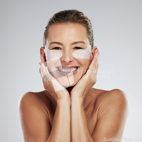 Image of Skincare, portrait and woman doing face cosmetics, smile and makeup with grey studio background. Facial, mature lady and older female relax, happy and with eye patch, collagen and confidence in skin.